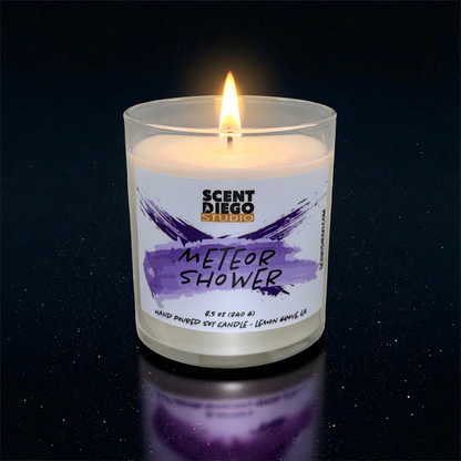Candle labeled 'Meteor Shower' by Scented Diego Studio on a dark background.  This candle is lit.