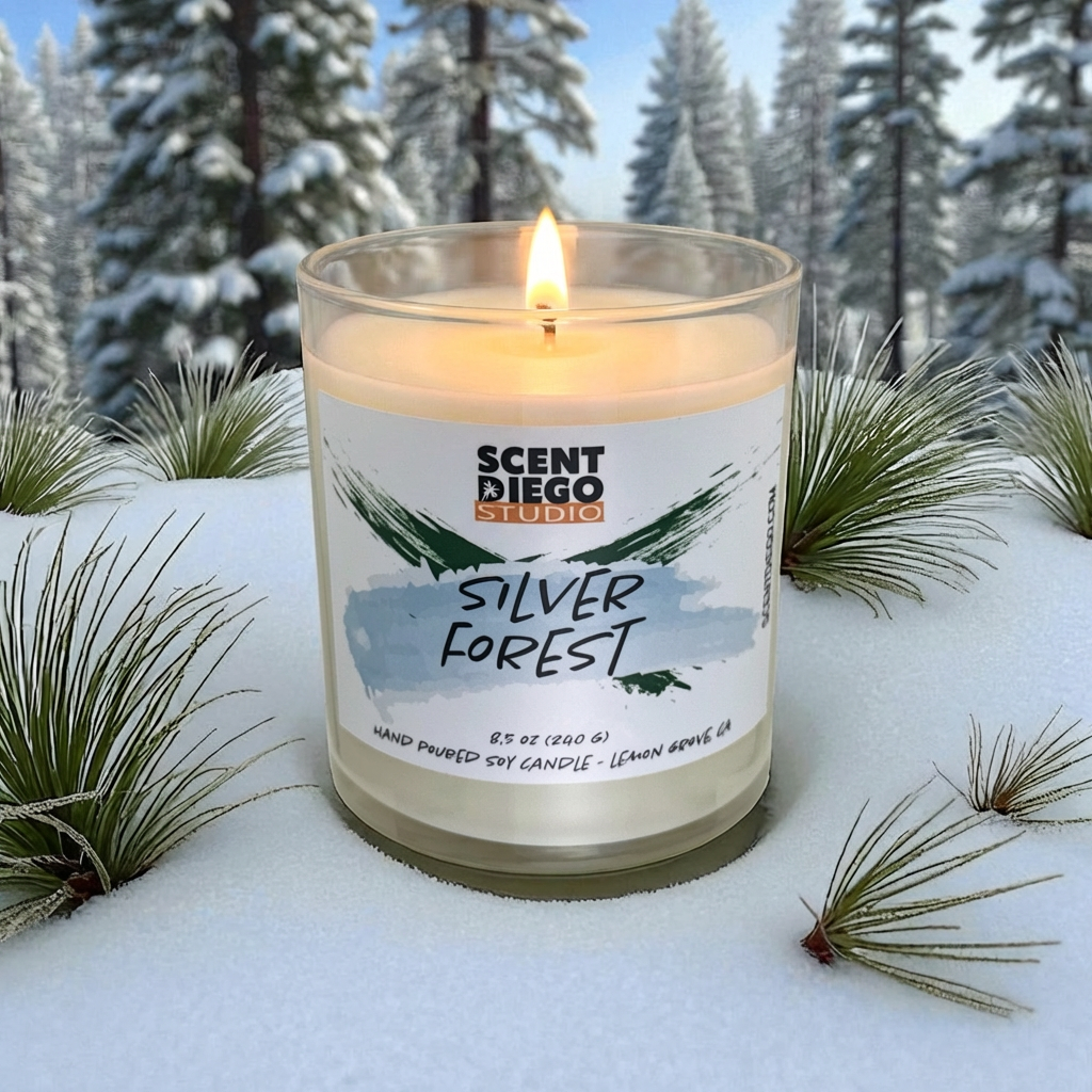 Candle labeled 'Silver Forest' by Scented Diego Studio in a snowy forest setting.  The candle is lit and with a flame.