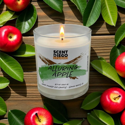 Candle labeled 'Alluring Apple' by Scent Diego Studio surrounded by red apples and green leaves on a wooden surface. This candle has a flame and no lid.